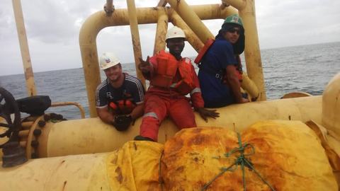 Crew in PPE seated on a yellow subsea mooring structure at sea